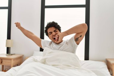 Genç İspanyol adam uyandığında kollarını uzatarak yatak odasında oturuyor..