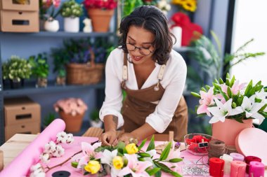 Young beautiful hispanic woman florist make bouquet of flowers at flower shop