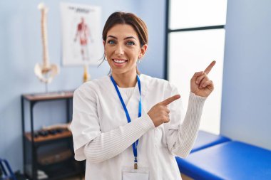 Genç esmer kadın ağrı kesici kliniğinde çalışıyor gülümsüyor ve kameraya bakıyor. İki eli ve parmağı yanda.. 