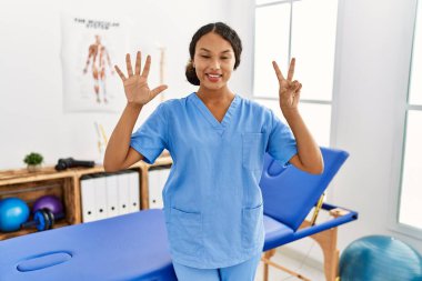 Ağrı kesici kliniğindeki güzel İspanyol fizyoterapist kadın yedi numarayı gösterip işaret ederken kendine güvenen ve mutlu bir şekilde gülümsüyor.. 