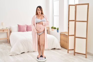Pregnant woman on weight machine making fish face with mouth and squinting eyes, crazy and comical. 