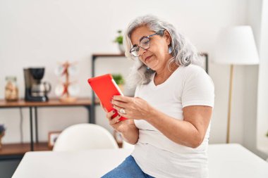 Middle age woman using touchpad sitting on table at home
