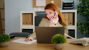 Genç kızıl saçlı iş kadını ofiste bilgisayarla konuşuyor.