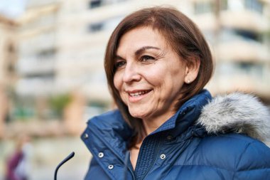 Orta yaşlı bir kadın elinde bardaklarla caddeye bakıyor.