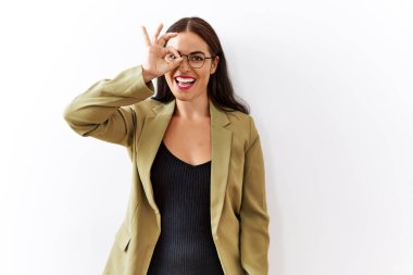 Genç esmer kadın izole edilmiş arka planda duruyor. El hareketleriyle gülümsüyor, gözleriyle gülen parmaklarının arasından bakıyor.. 