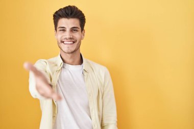 Sarı arka planda duran genç İspanyol adam gülümsüyor. Avuç içi dolusu yardım ve kabullenme teklif ediyor.. 