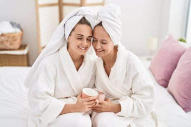 Two women mother and daughter wearing bathrobe drinking coffee at bedroom