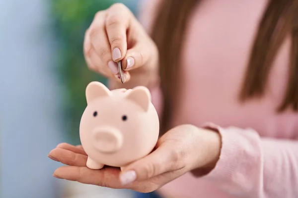 Jovem Mulher Inserindo Moeda Banco Porquinho Casa — Fotografia de Stock