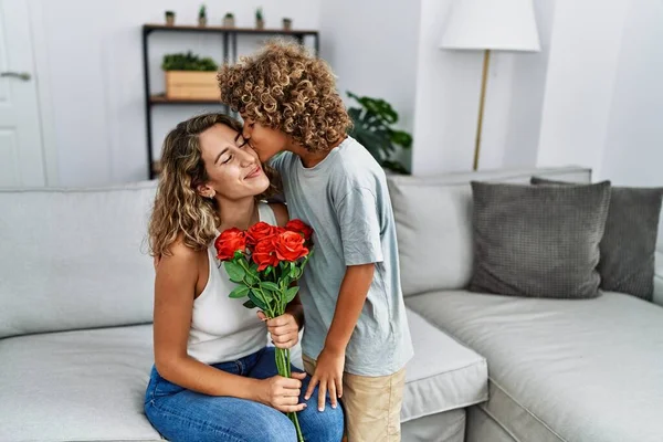 Mother and son kissing and hugging each other holding flowers at home