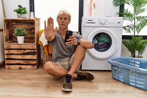 Young Blond Man Doing Laundry Using Smartphone Doing Stop Sing — Stok fotoğraf