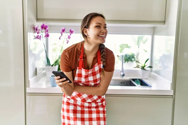 Νεαρή Όμορφη Ισπανίδα Γυναίκα Φορώντας Ποδιά Χρησιμοποιώντας Smartphone Στην Κουζίνα — Φωτογραφία Αρχείου