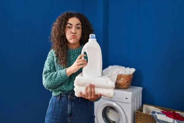 Young Hispanic Woman Holding Laundry Detergent Bottle Puffing Cheeks Funny — Stock fotografie