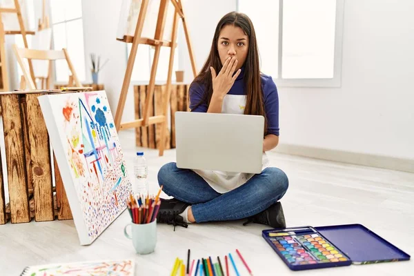 年轻的黑发女子手捂着笔记本电脑坐在艺术工作室的地板上 既震惊又害怕犯错 惊讶的表情 — 图库照片