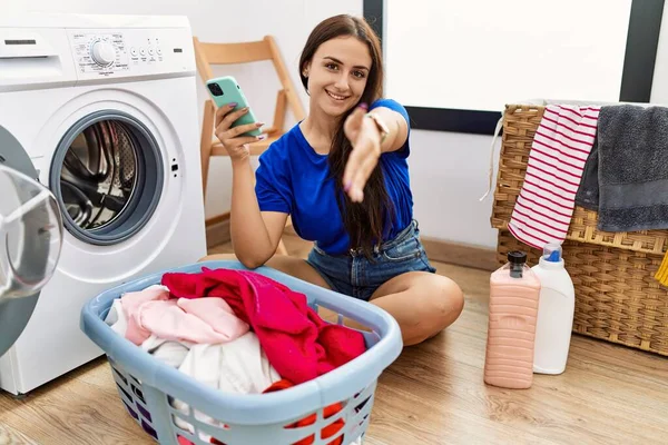 Genç Esmer Kadın Çamaşır Yıkıyor Akıllı Telefon Kullanıyor Gülümsüyor Dostça — Stok fotoğraf