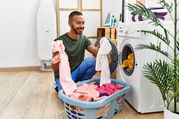 Young hispanic man cleaning clothes using washing machine at laundry