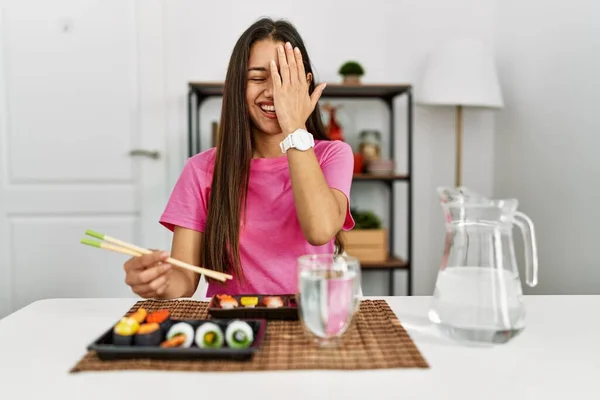 年轻的黑发女人用筷子捂住一只眼睛吃寿司 脸上带着自信的微笑 还有令人惊讶的情绪 — 图库照片