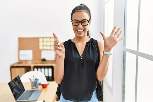 Young hispanic business woman working at the office showing and pointing up with fingers number six while smiling confident and happy.