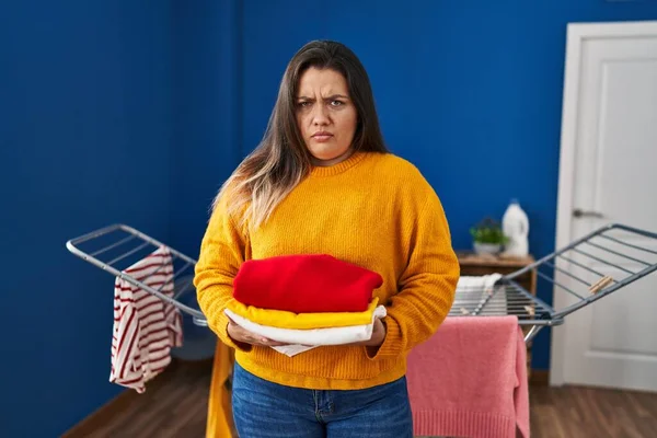 Young Hispanic Woman Holding Clean Folded Laundry Skeptic Nervous Frowning — Stock Photo, Image