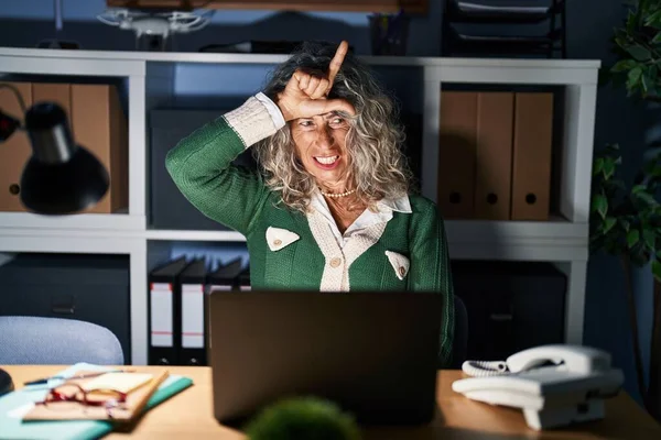 中年女性仕事で夜に使用してコンピュータラップトップ作り楽しいです人々とともに指で額を行います負け犬ジェスチャーモックと侮辱 — ストック写真