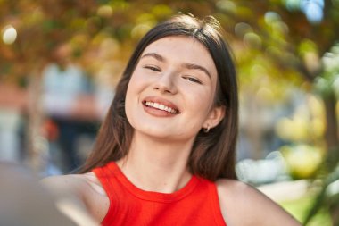 Beyaz kadın gülümsüyor. Parkta kamerayla özçekim yapıyor.