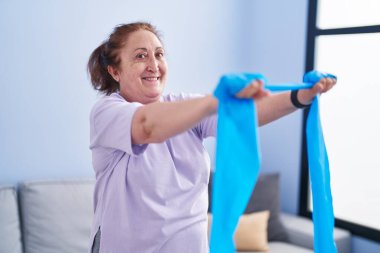 Senior woman smiling confident using elastic band training at home