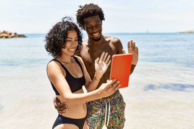 Genç ırklar arası turist çifti sahilde touchpad kullanarak görüntülü görüşme yapıyorlar..