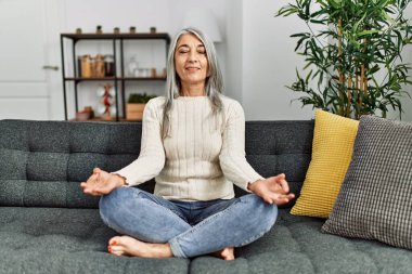 Orta yaşlı, kır saçlı, gülümseyen, yoga egzersizi yapan bir kadın.