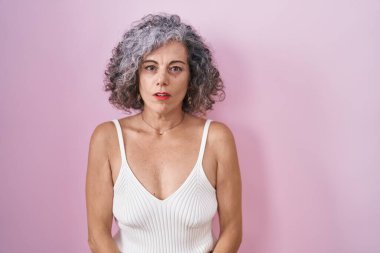 Middle age woman with grey hair standing over pink background looking sleepy and tired, exhausted for fatigue and hangover, lazy eyes in the morning. 