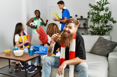 Genç futbol holiganı gülümseyerek evde bira içiyor..