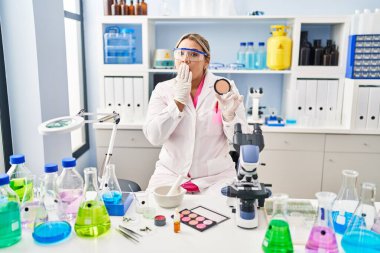 Young hispanic woman working at scientist laboratory doing make up covering mouth with hand, shocked and afraid for mistake. surprised expression 