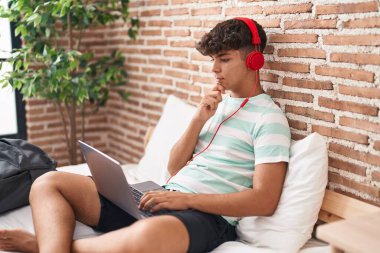 Evde dizüstü bilgisayar kullanan İspanyol bir genç yatak odasında oturmuş ciddi bir yüz ifadesiyle eli çenesinde soru soruyor, kafa karıştırıcı bir fikir hakkında düşünceli. 