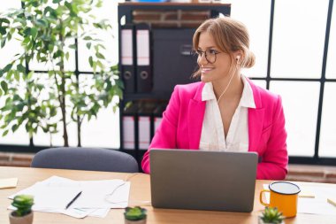 Young blonde girl business worker using laptop and earphones working at office