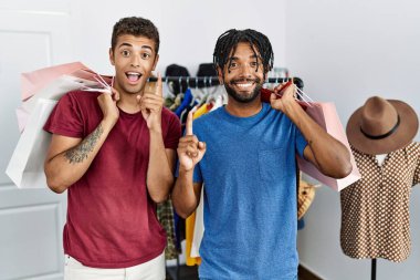 Young hispanic men holding shopping bags at fashion boutique surprised with an idea or question pointing finger with happy face, number one 