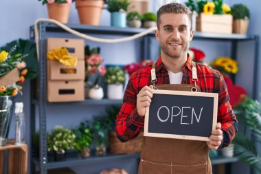 Young caucasian man working at florist holding open sign smiling with a happy and cool smile on face. showing teeth. 