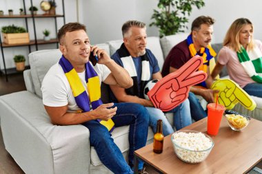 Group of middle age friends watching and supporting soccer match talking on the smartphone at home.