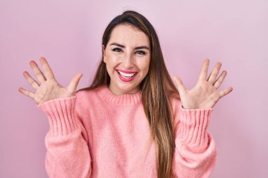 Pembe arka planda duran genç İspanyol kadın on numarayı gösterip işaret ederken kendinden emin ve mutlu bir şekilde gülümsüyor.. 