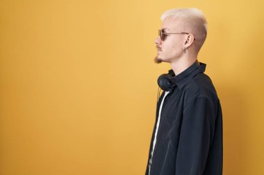 Sarı arka planda duran güneş gözlüğü takan genç beyaz adam, yan tarafa bakıyor, rahat bir poz veriyor ve kendine güvenen bir gülümseme takınıyor.. 