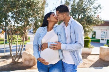 Genç Latin çift bebek bekliyor. Birbirlerine sarılıyorlar ve parkta öpüşüyorlar.