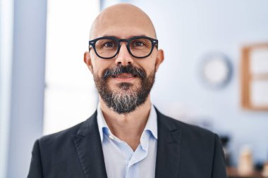 Genç kel iş adamı ofiste kendinden emin gülümsüyor.