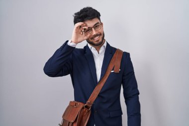 Sakallı İspanyol bir adam iş kıyafetleri giyiyor. El hareketleriyle gülümsüyor ve mutlu yüzüyle parmaklarının arasından bakıyor.. 