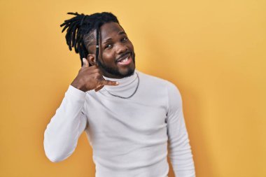 Sarı arka planda balıkçı yaka kazak giyen Afrikalı adam telefonla el ve parmaklarıyla telefonla konuşuyor gibi gülümsüyor. iletişim kavramları. 