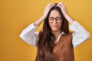 Sarı arka planda duran genç esmer kadın. Gözlük takıyor. Baş ağrısı çekiyor. Eller başının üstünde.. 