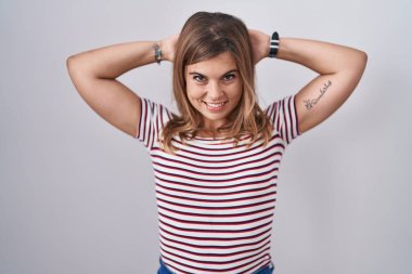 Young hispanic woman standing over isolated background relaxing and stretching, arms and hands behind head and neck smiling happy 
