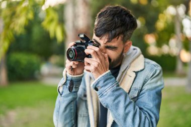 Young hispanic man using professional camera at park