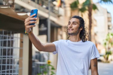 Young hispanic man smiling confident making selfie by the smartphone at coffee shop terrace