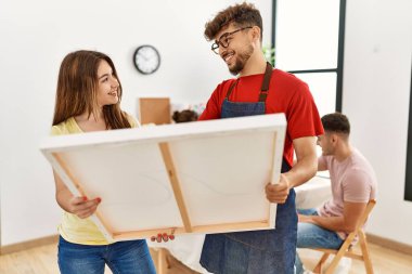 Group of people drawing sitting on the table. Man and woman smiling happy holding canvas at art studio.