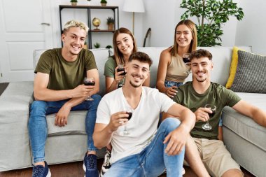 Group of young friends smiling happy drinking red wine at home.