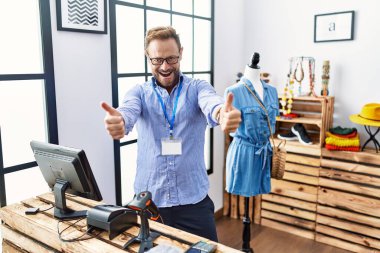 Perakende satış mağazasında müdürlük yapan orta yaşlı bir adam elle olumlu jest yapmayı onaylıyor. Gülümsüyor ve başarı için seviniyor. kazanan jest. 
