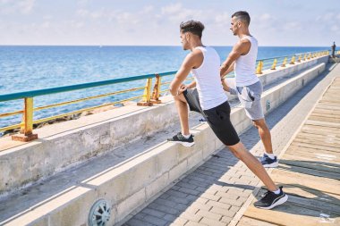 Two hispanic men couple stretching at seaside