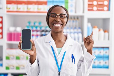 Eczanede çalışan Afrikalı Amerikalı bir kadın akıllı telefon ekranında gülümsüyor. 